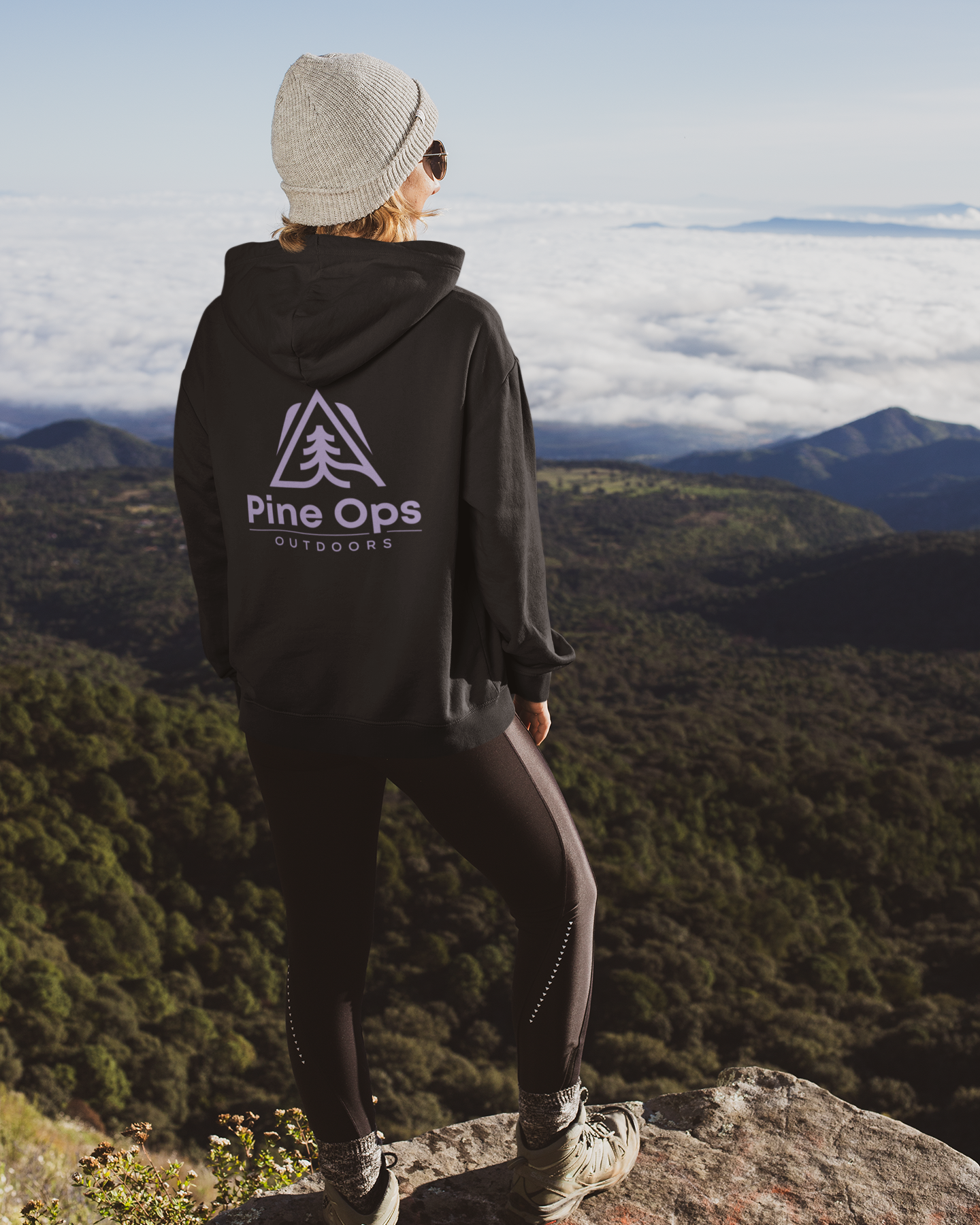 Person wearing a black hoodie with 'Pine Ops Outdoors' logo, standing on a mountain overlooking a forested valley.