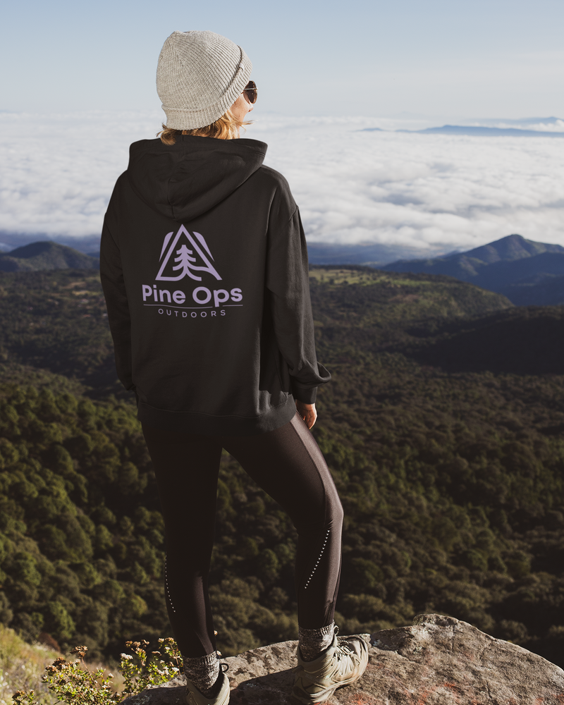 Person wearing a black hoodie with 'Pine Ops Outdoors' logo, standing on a mountain overlooking a forested valley.