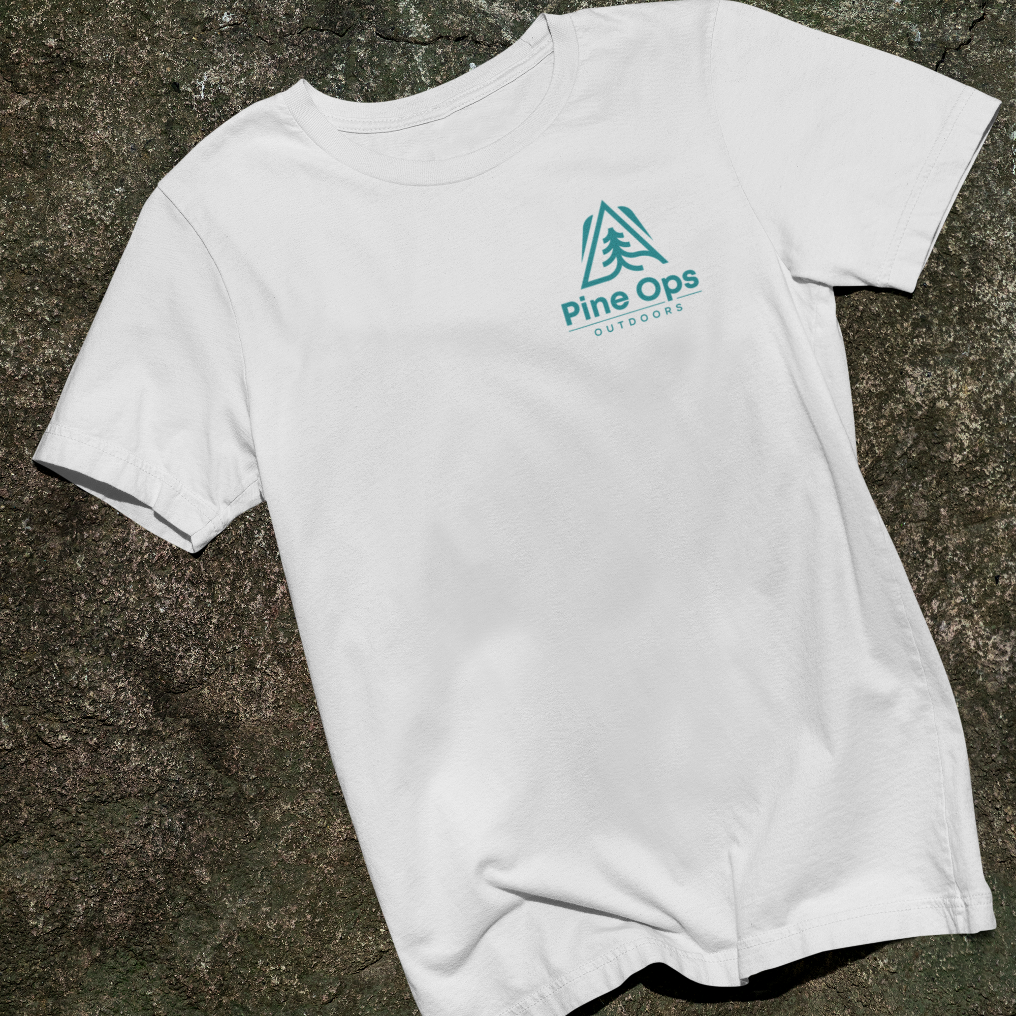 White t-shirt with Pine Ops logo on a stone surface