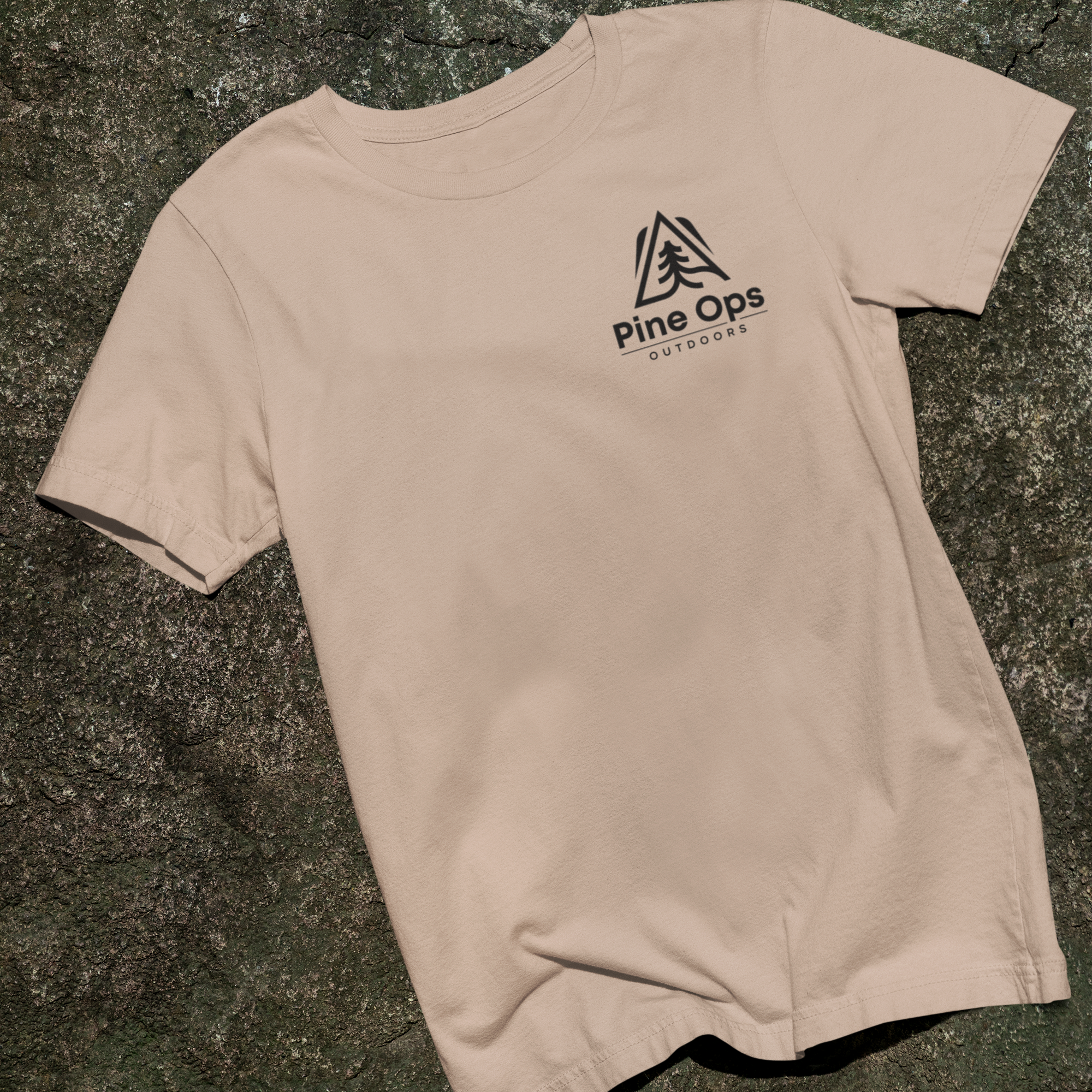 Beige pine ops outdoors t-shirt with a logo on the back, placed on a textured surface.